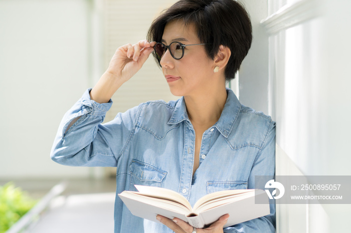 A smart looking middle aged woman resting her eyes from reading book. She’s in her 40s and have long-sightedness, she wearing eyeglasses with progressive lens. Eyes problem, Hyperopia, Sore and tired.