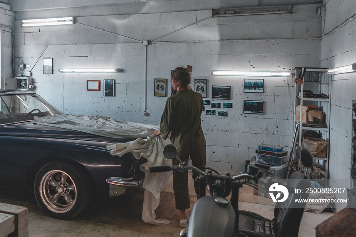 Attractive Caucasian female removing cover from her vintage old car in a garage