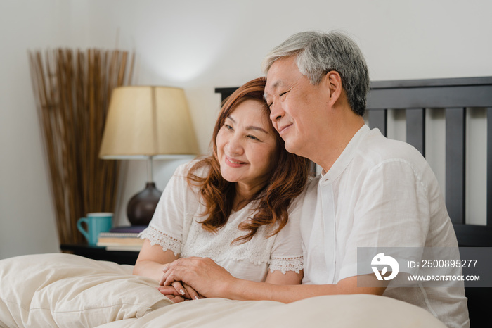 Asian senior couple talking on bed at home. Asian Senior Chinese grandparents, husband and wife happy relax together after wake up while lying on bed in bedroom at home in the morning concept.