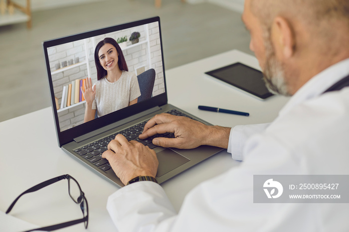 Doctor and patient online. Girl patient says consults using laptop webcam with senior man doctor at virtual clinic.