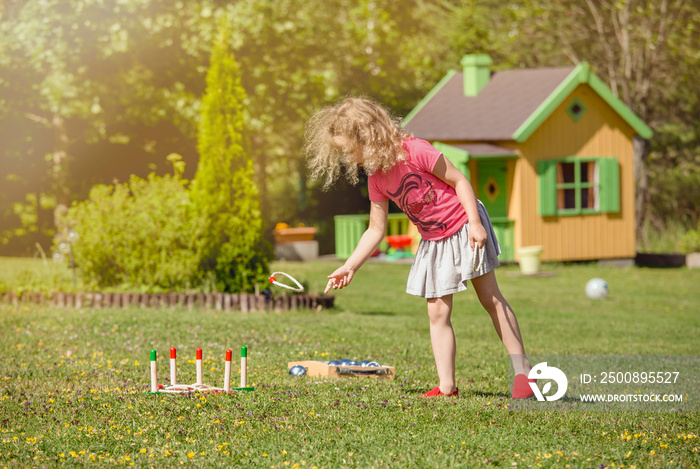 Cute 6 year old child girl play rope peg throwing game in home garden outdoors on sunny summer day. Leisure activity concept.