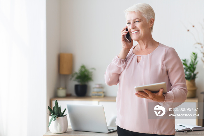 Busy old woman consulting client on phone, using tablet