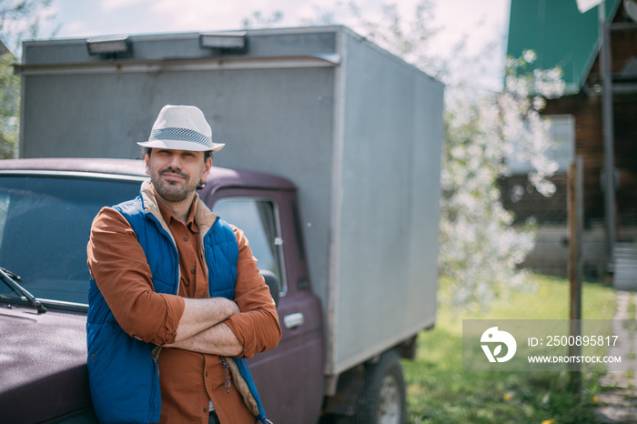 A young male farmer in work clothes next to a small truck. The concept of delivery of farm products and small business.