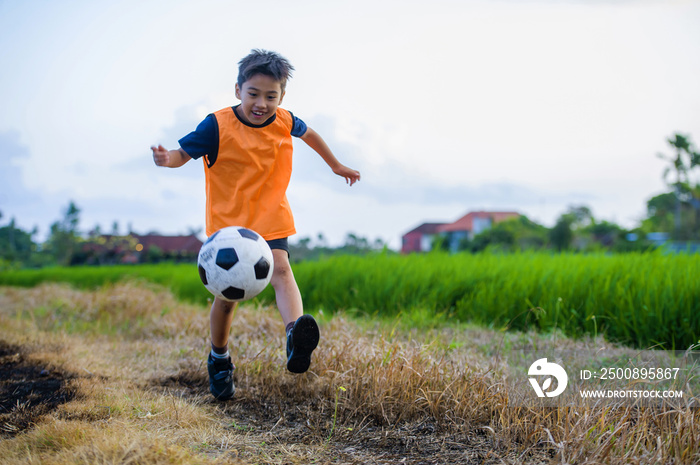 8 or 9 years old happy and excited kid playing football outdoors in garden wearing training vest running and kicking soccer ball