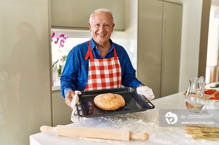 Senior man holding oven tray with homemade bread at kitchen