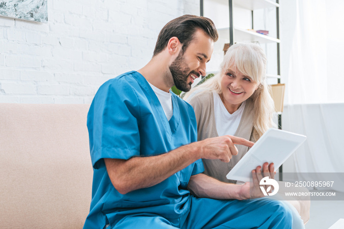 happy young caregiver and senior woman using digital tablet together