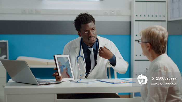 Doctor and senior patient looking at heart picture on modern tablet screen for examination and understanding cardiology. Sick old woman and medic analyzing virtual cardiogram at desk