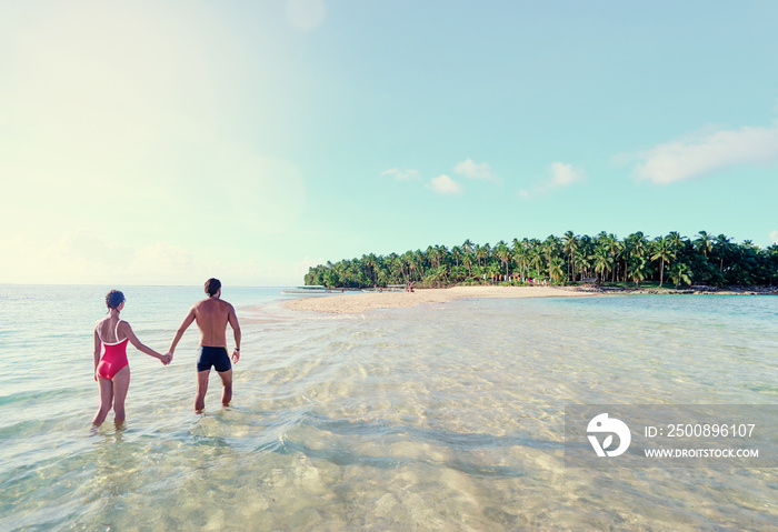 Honey moon on the sea shore. Back view of loving couple walking together on beautiful tropical white sand beach.