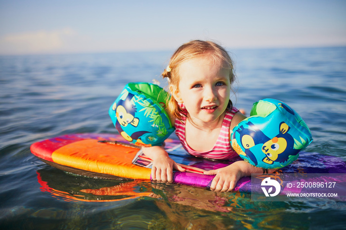 Happy little girl swimming with water wings in Mediterranean sea in France