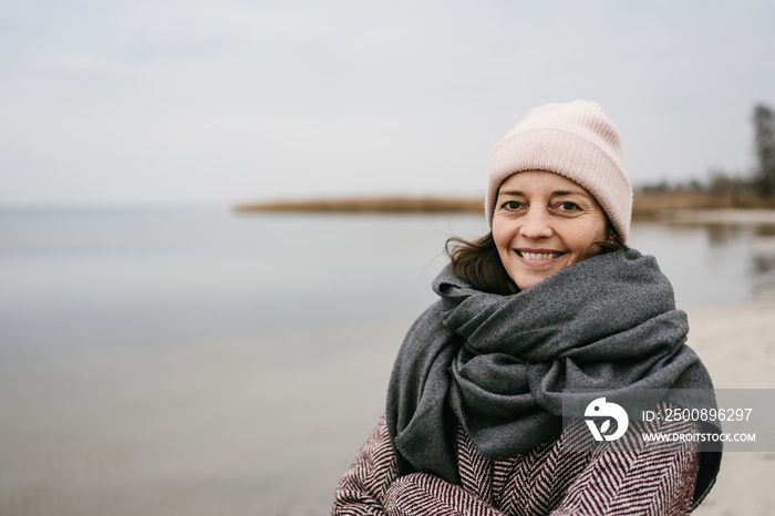 middle aged woman standing by the sea in winter with a gray scarf and looking into the camera