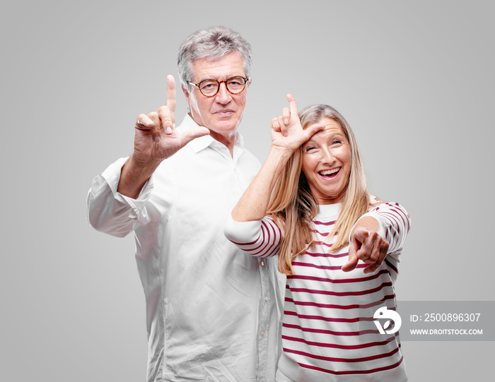 senior cool husband and wife gesturing  loser  with fingers mockingly, with a happy, proud, and self-satisfied look.