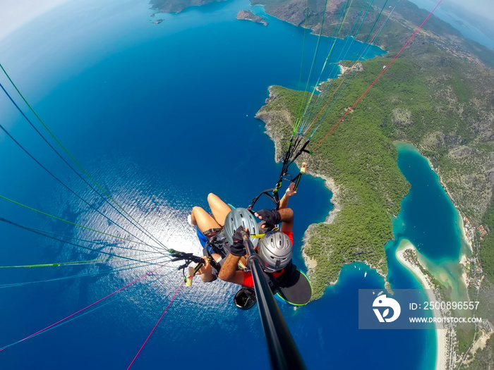 Paraglider tandem flying over the sea with blue water and mountains in bright sunny day. Aerial view of paraglider and Blue Lagoon in Oludeniz, Turkey. Extreme sport. Landscape