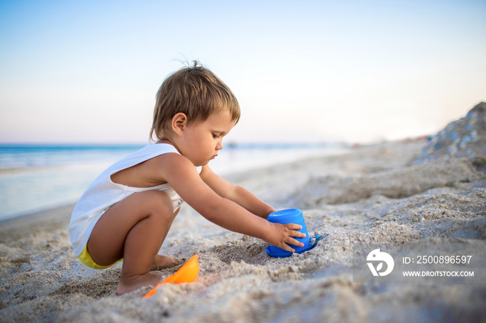 Boy playing with toys on the beach building beads and turrets smiling at someone behind the scenes on summer vacation