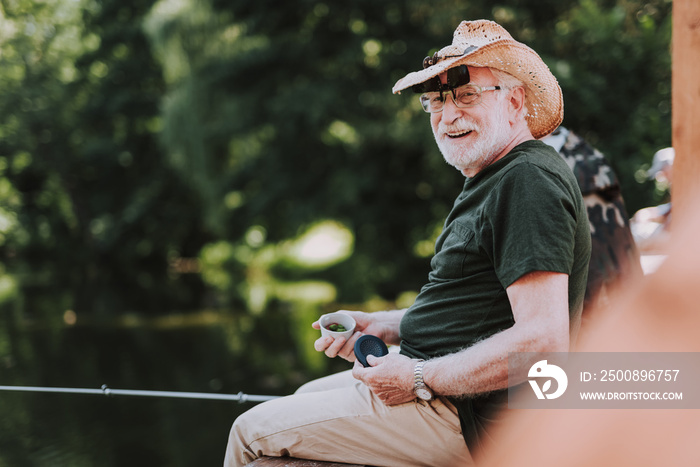 Positive elderly man enjoying his fishing weekend while holdign a rod