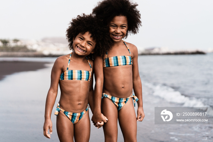 Happy african sister twins running on the beach together - Focus on faces