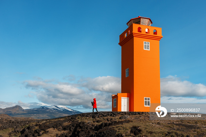 A tourist girl in a red jacket looks at the Svortuloft Lighthouse in Snaefellsnes National Park, Iceland.