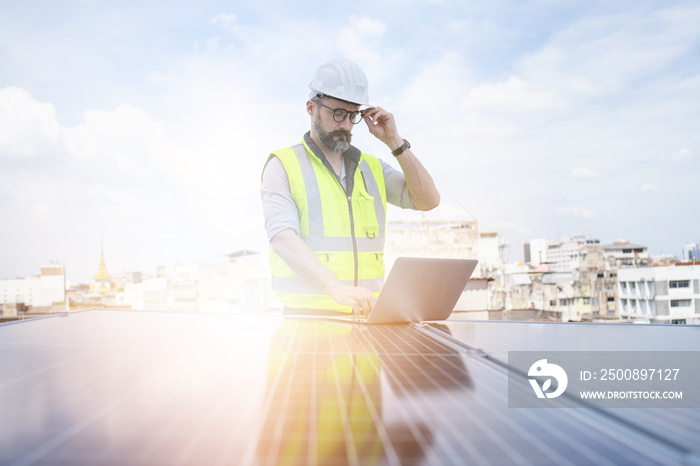 Rooftop solar power plant engineers sitting and examining photovoltaic panels. Concept of alternative energy and its service. Electrical and instrument technician use laptop to maintenance electric sy