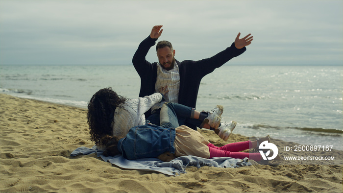 Family play tickle beach. Mom dad child hugging lying on sea shore sand picnic.