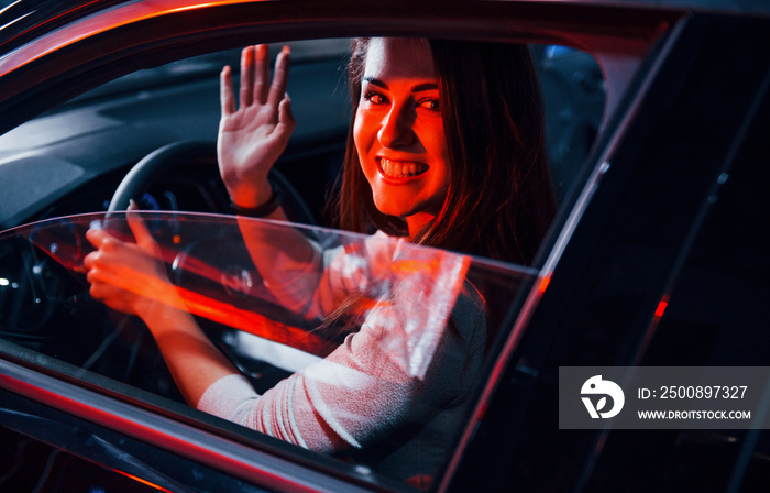 Young woman is inside of brand new modern automobile with red lighting