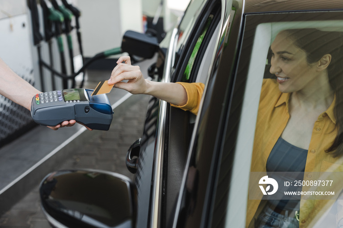 Selective focus of worker of gas station holding payment terminal near smiling woman paying with credit card in car