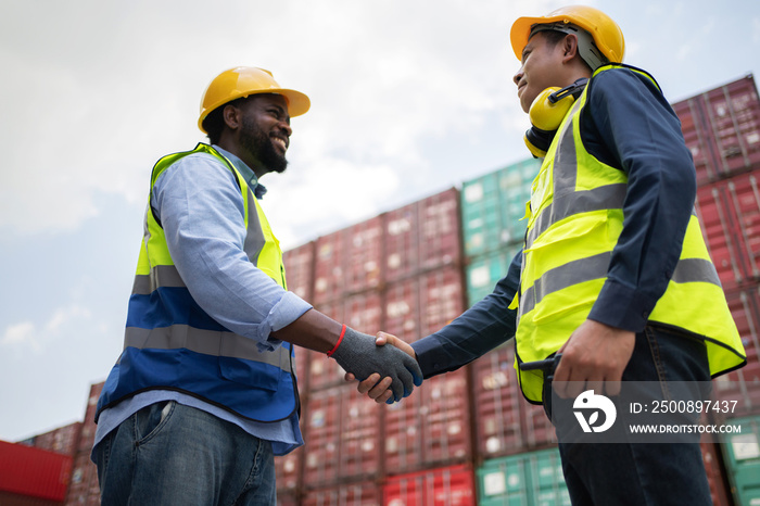 Dock manager and engineer worker shake hand with smile in shipping container yard. Import and export product. Manufacturing transportation and global business concept. Selective focus at hand