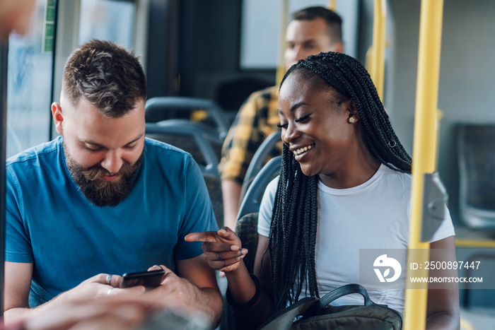 Multiracial friends talking while riding a bus in the city and using a smartphone