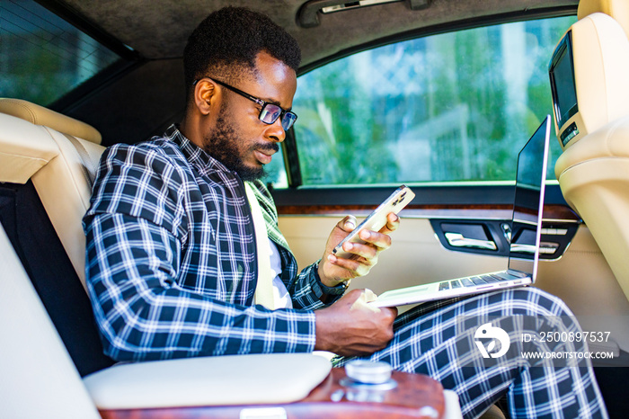 Handsome successful rich african american businessmen in a stylish suit and sitting in a luxury car and works with laptop