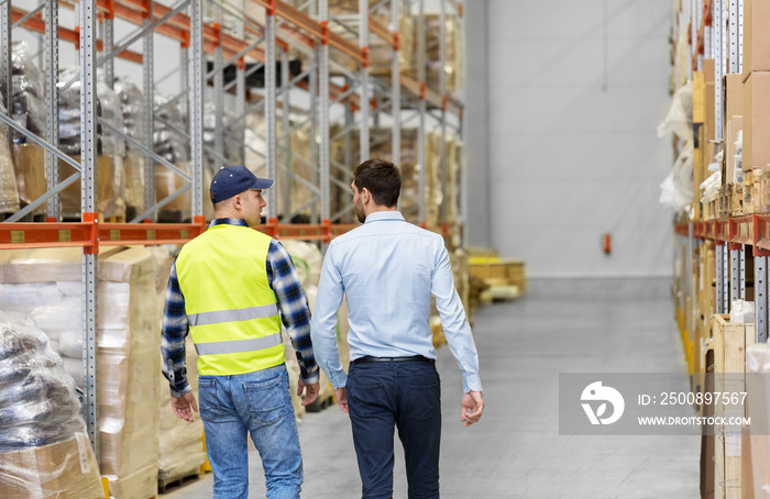 logistic business and people concept - worker and businessman walking along warehouse