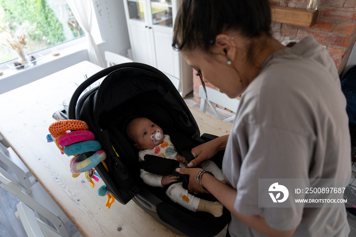 Mother fastening seat belts in car safety seat at home