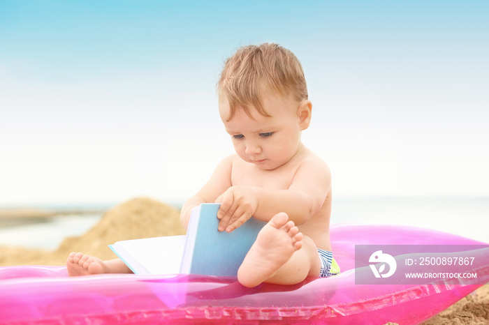 Cute baby boy sitting on inflatable mattress at beach