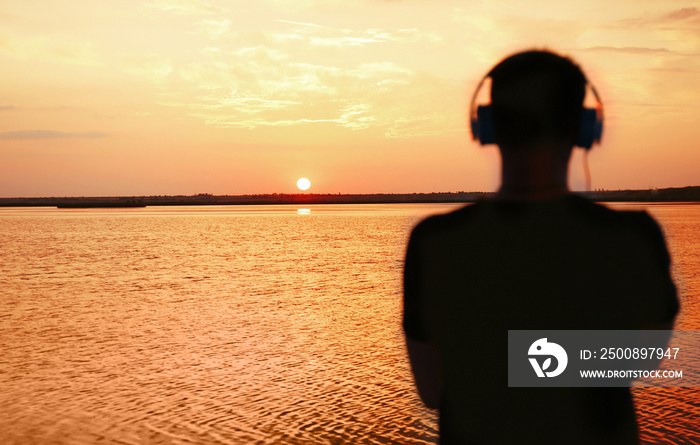 Silhouette of man with headphones on sunset sky background