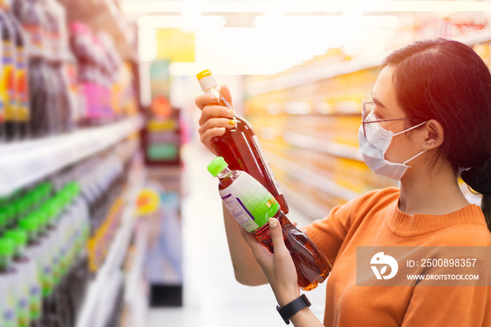 Asian Customer shopping in supermarket with face mask choice select and compare fish sauce by reading products detail label on shelf