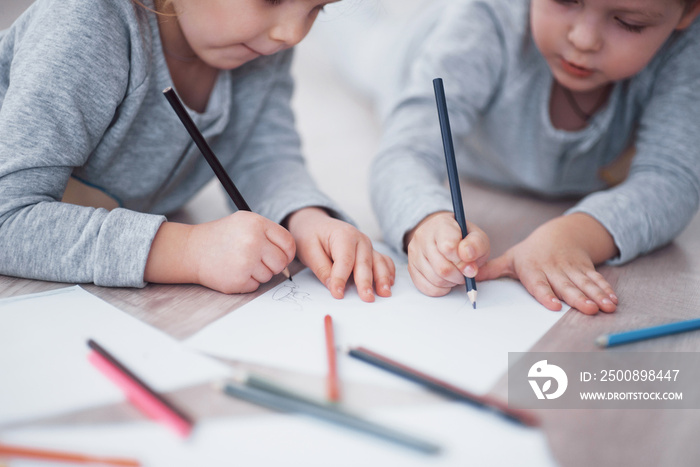 Children lie on the floor in pajamas and draw with pencils. Cute child painting by pencils.Hand of child girl and boy draw and paint with crayon. Close up view