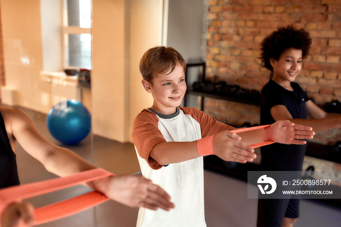 Caucasian boy working out using resistance band together with other kids in gym. Sport, healthy lifestyle, physical education concept