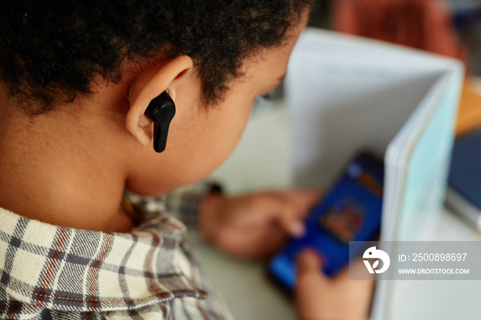 Close up of black kid listening to music during school class and hiding phone, copy space