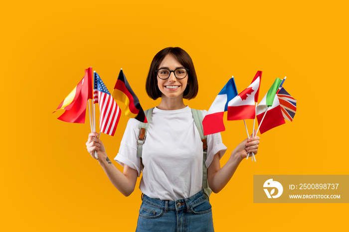 Happy lady showing bunch of diverse flags cheerfully smiling at camera over yellow studio background