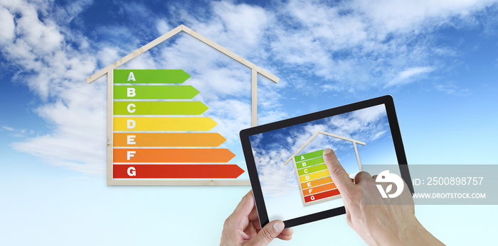 hand touch screen of digital tablet with house shape and energy efficiency chart symbol, isolated on blu sky background, green buildings and save energy eco sustainability