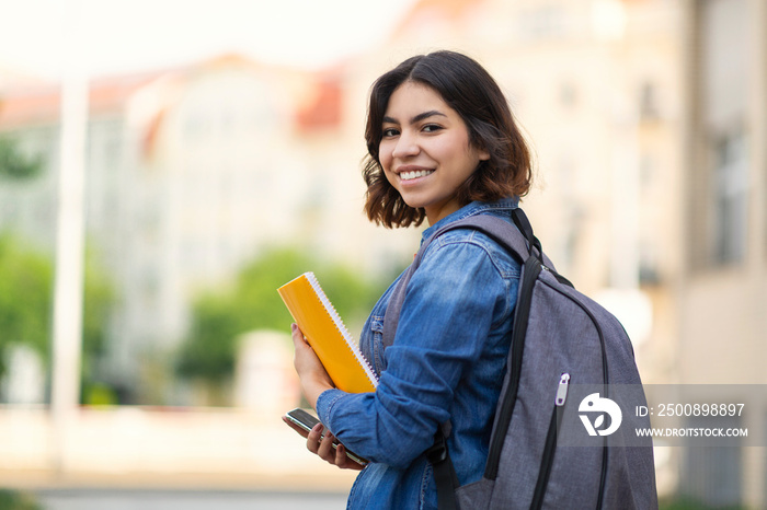 Smiling Young Arab Female Student With Workbooks And Backpack Standing Outdoors