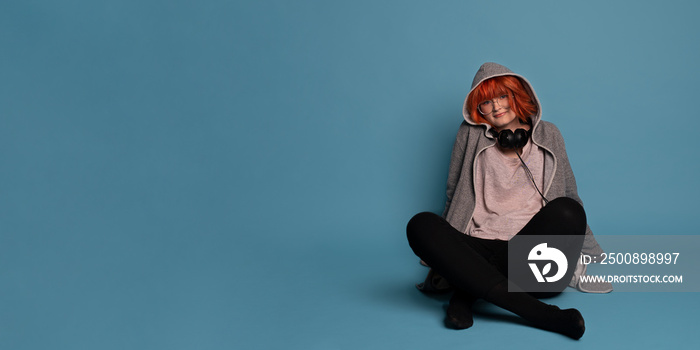 Photography of stylish teenage girl with makeup in headphones on blue background.Large banner with negative space.