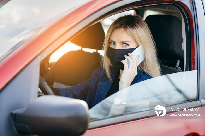 Young girl in a black mask sitting in a car and talking on the phone, protective mask against coronavirus