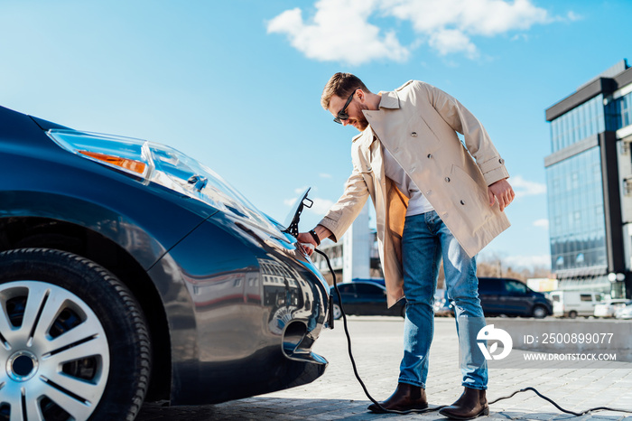 Stylish man in sunglasses disconnects the charging cable from his electric car