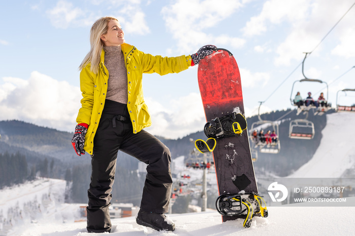 Young woman with snowboard on the slope of hill at winter resort