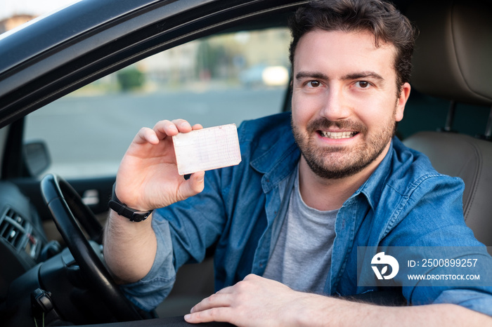 Cheerful man holding driver license in his car