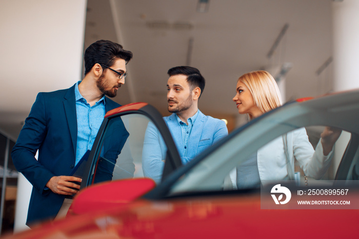 Young couple choosing new car for buying in dealership shop