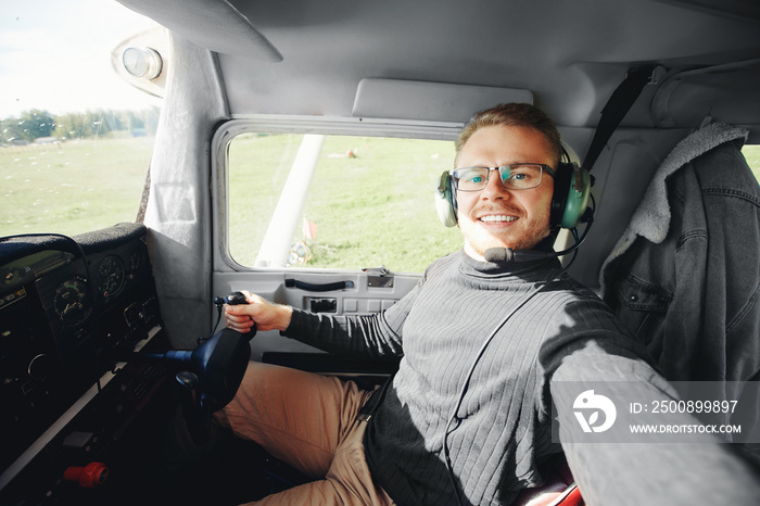 Selfie photo happy man pilot in light aircraft cockpit, aviator headset and steering wheel