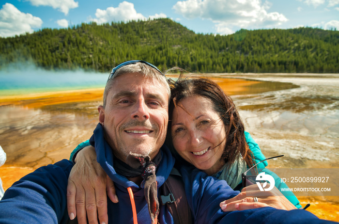 Happy couple making a selfie with the background of Grand Prismatic Spring Geyser, Yellowstone National Park