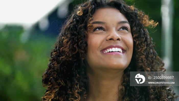 Happy African American woman closeup face looking up at sky smiling. One hopeful black hispanic 20s adult girl