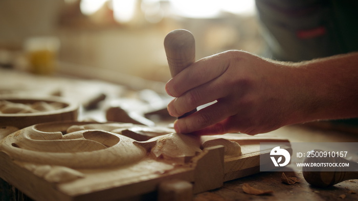 Unknown man decorating wood indoors. Guy carving ornament in carpentry workshop