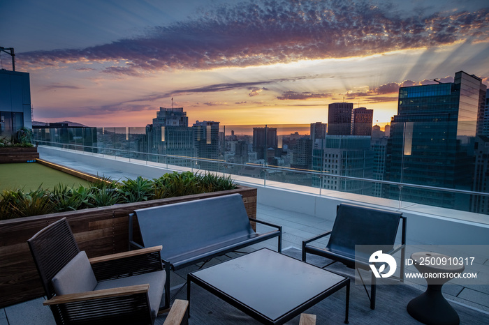 A rooftop deck with chairs overlooks the San Francisco skyline sunset with purple and gold clouds