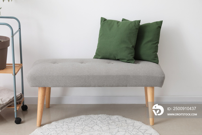 Soft bench with green pillows near light wall